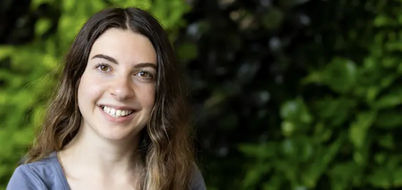 Woman smiling in front of a green wall of plants.