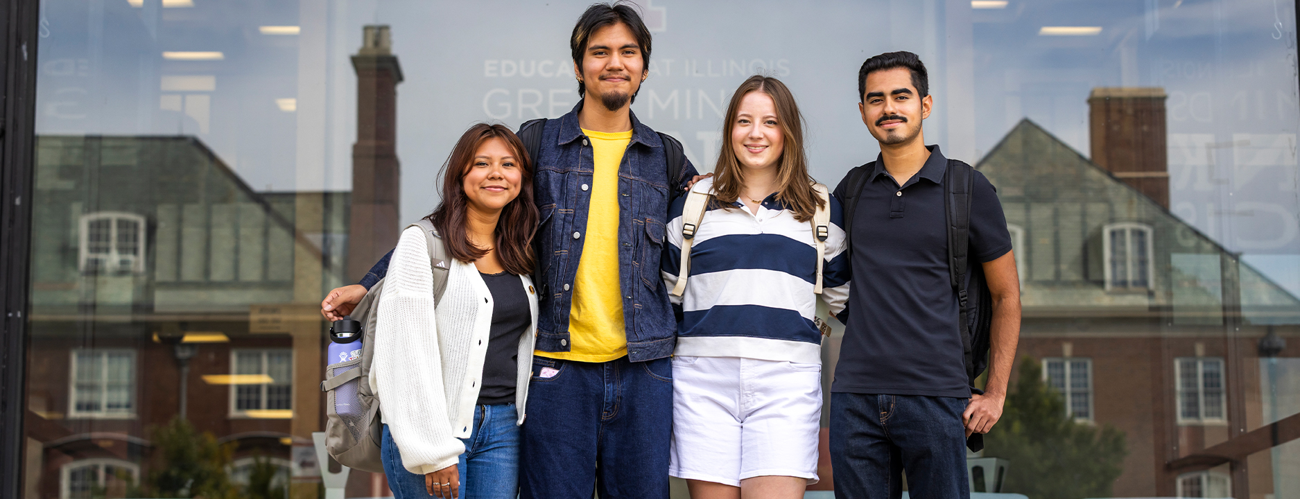 Four undergraduate students smiling and embracing in front of the college of education