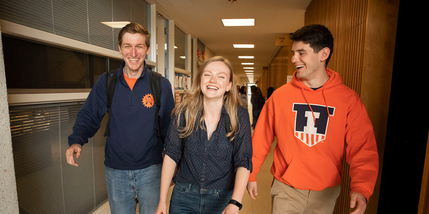Three students smiling walking down the College of Education hallway