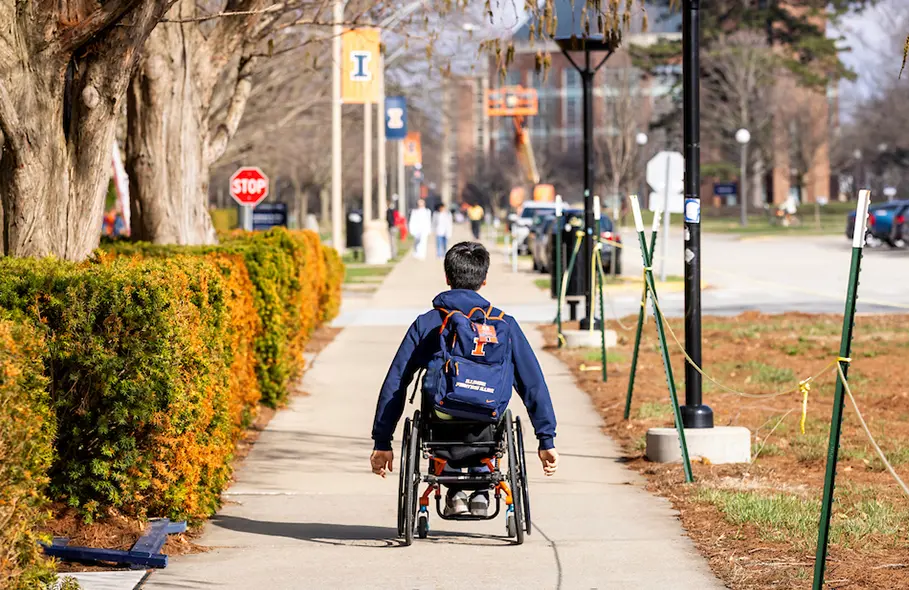 A student heads to class in their wheelchair with an illinois backpack on