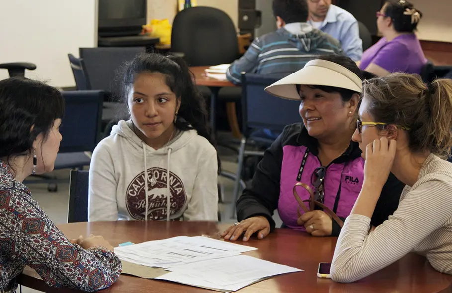 Teacher, student, parent and interpreter sit at a table together.