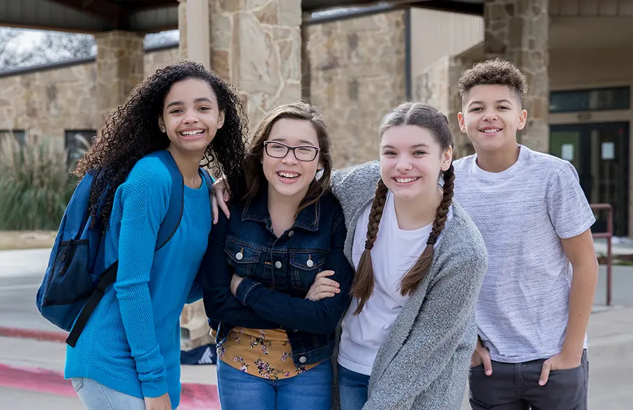 Four students grinning in front of a building