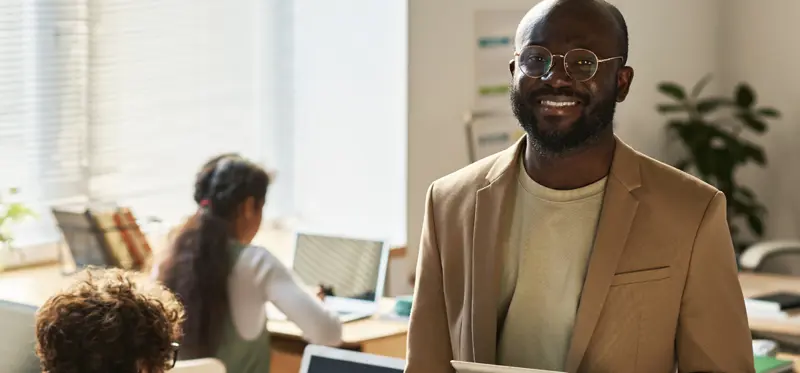 Male person with glasses smiling in a classroom
